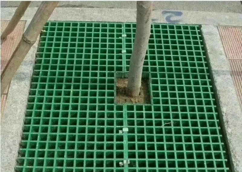Green molded FRP grating panels cut around a tree opening and laid in a paved tree pit