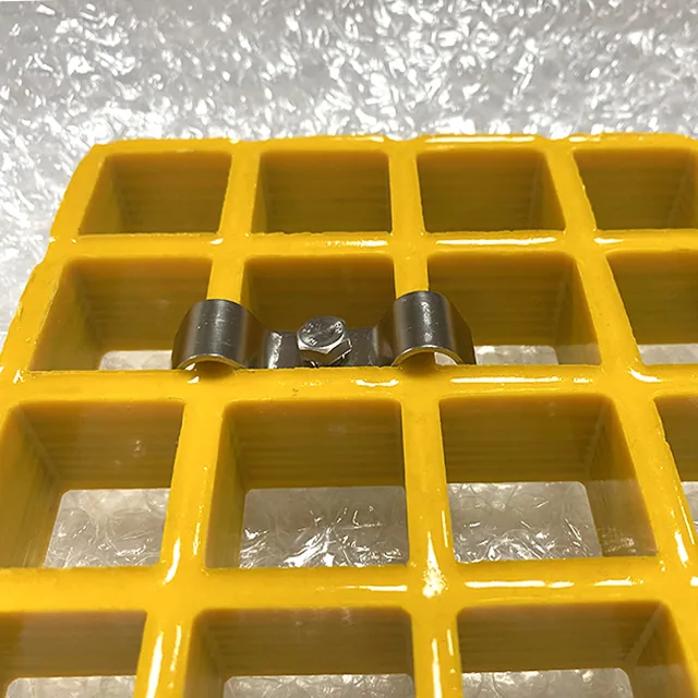 Metal M clip fitted across two adjacent bars of a yellow molded FRP grating panel with a bolt through the center