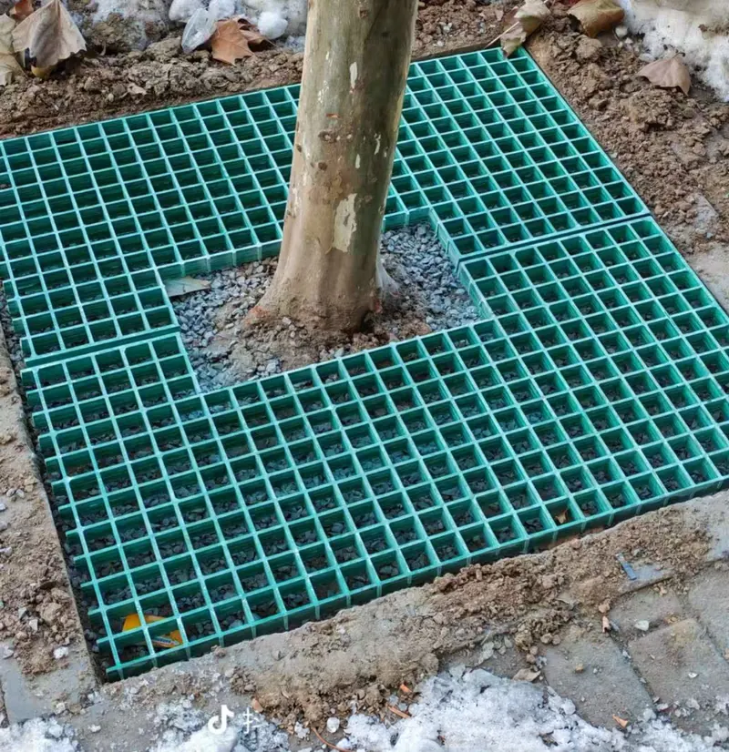 Green FRP tree-surround grating with a shaped opening around a tree trunk