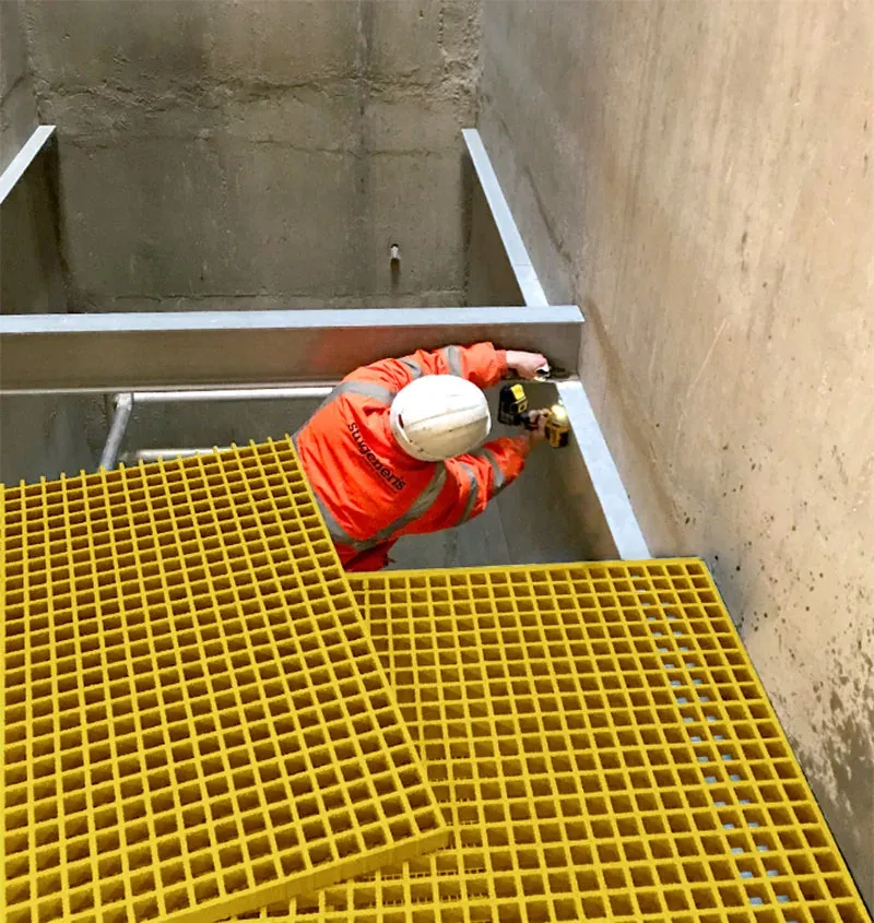 Worker installing FRP grating over a framed opening at a construction site