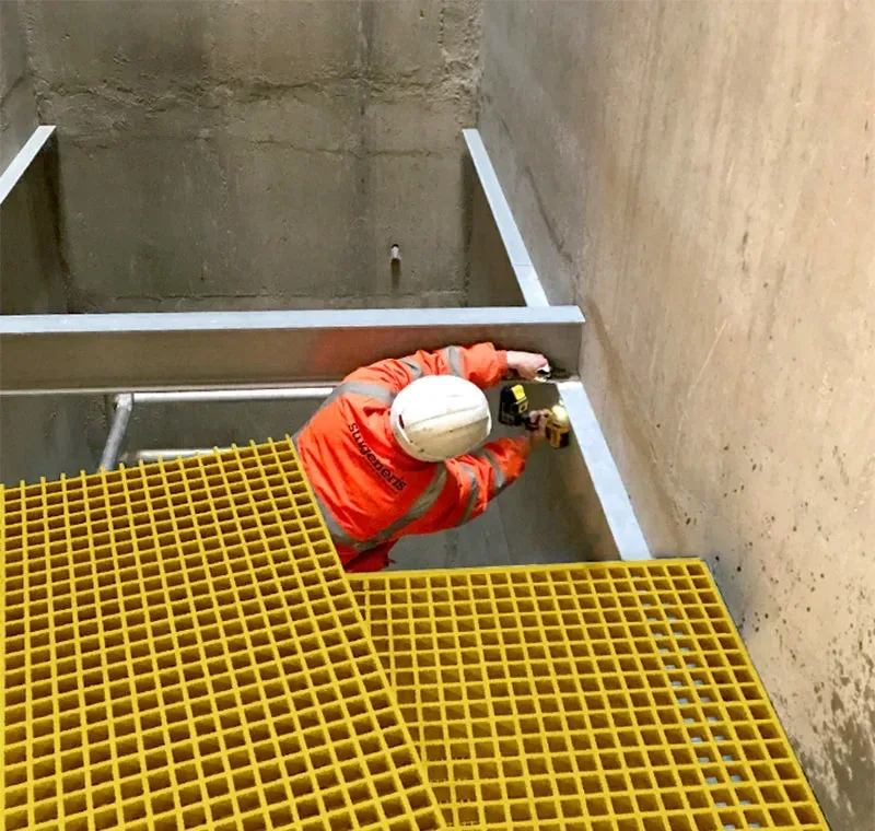 Worker fitting yellow FRP grating covers into a framed concrete trench opening
